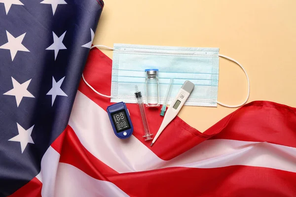 Pulse oximeter, medical mask, vaccine, syringes and USA flag on beige background