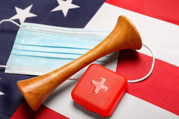Stethoscope with medical mask and pill container on USA flag, closeup