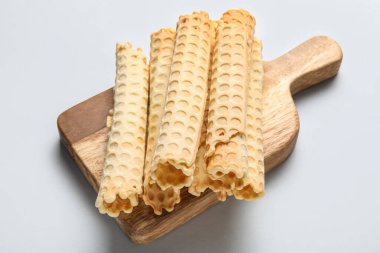 Board with delicious wafer rolls on grey background