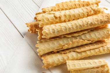 Parchment with delicious wafer rolls on white wooden background