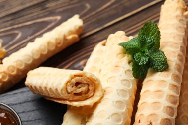 Delicious wafer rolls with mint on brown wooden background