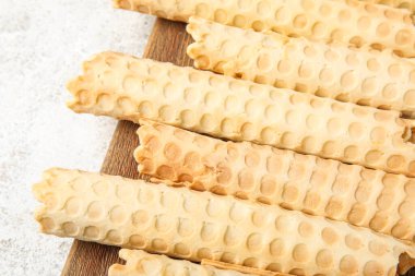 Board with delicious wafer rolls on white grunge background