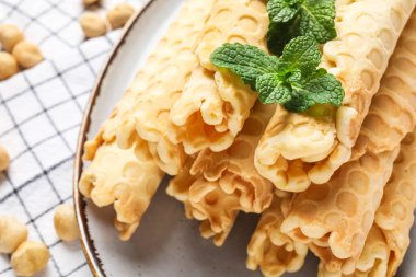 Plate with delicious wafer rolls and mint on napkin, closeup