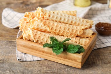 Board with delicious wafer rolls and mint on wooden background