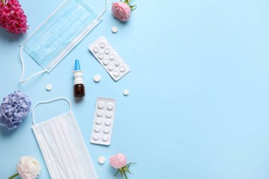 Mavi arka planda ilaç, çiçek ve tıbbi maskeli burun damlası. Mevsimsel alerji kavramı