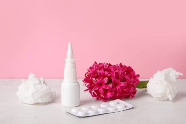 Nasal drops with pills, flower and tissues on table near pink wall. Seasonal allergy concept