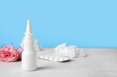 Nasal drops with pills, flowers and tissues on table near blue wall, closeup. Seasonal allergy concept