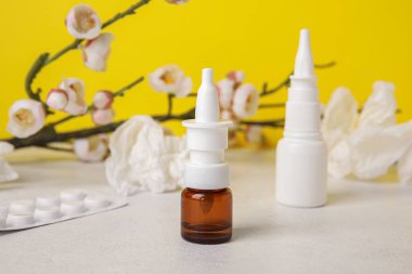 Nasal drops with pills, flowers and tissues on table near yellow wall, closeup. Seasonal allergy concept