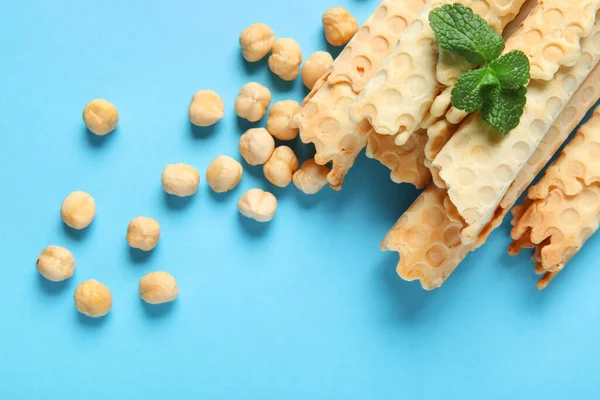Delicious wafer rolls, hazelnuts and mint on blue background