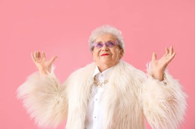 Happy senior woman in fur coat on pink background
