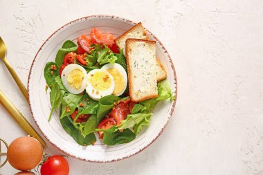 Plate of delicious salad with boiled eggs and salmon on white grunge background