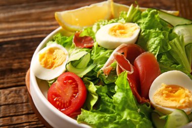 Plate of delicious salad with boiled eggs and jamon on brown wooden background
