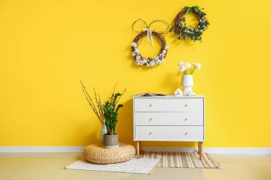 Interior of stylish room with Easter wreaths, drawers and vases