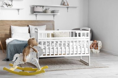 Interior of light bedroom with bed, baby crib and toys