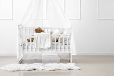 Baby crib with toy bear in light bedroom