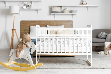 Interior of light bedroom with bed, baby crib and toys