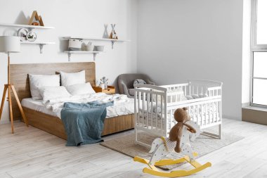 Interior of light bedroom with bed, baby crib and toys