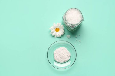 Bowl of body scrub, jar with sea salt and chamomile flower on color background
