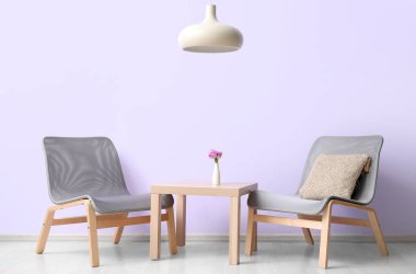 Stylish grey armchairs and table near lilac wall