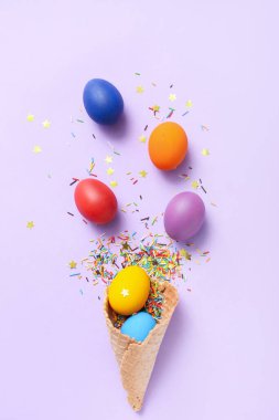 Wafer cone with Easter eggs and confetti on lilac background