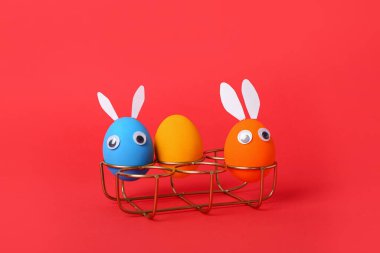 Holder with funny Easter eggs on red background