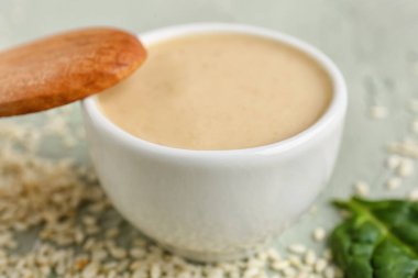 Bowl with tasty tahini on grunge background, closeup