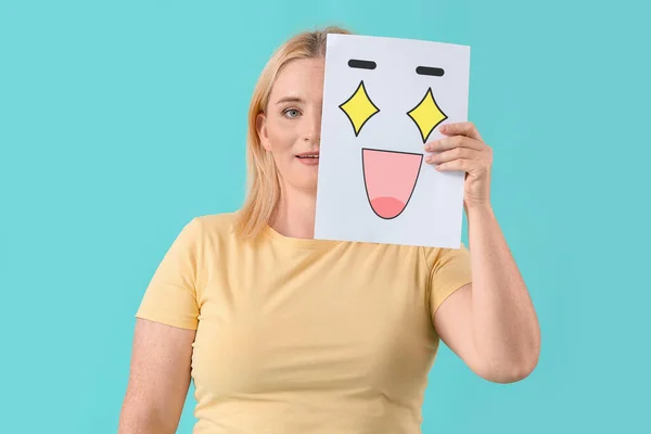 Woman holding paper with drawn happy emoticon on turquoise background