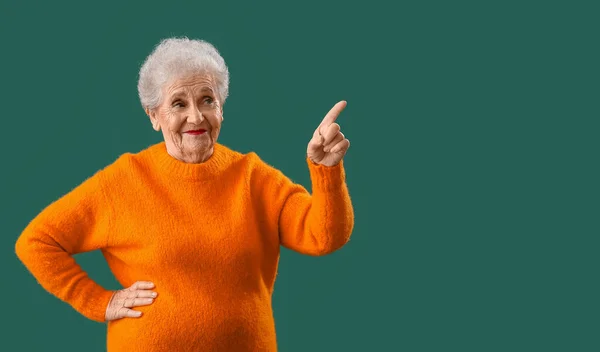 オレンジセーターのシニア女性で何かを指している緑の背景 — ストック写真