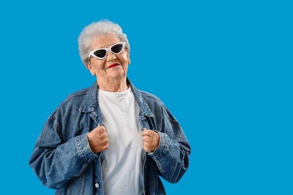 シニア女性でサングラスとデニムジャケット上の青の背景 — ストック写真