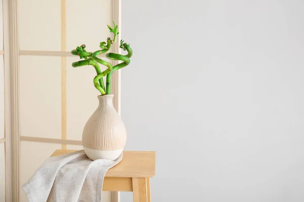 Folding screen and vase with bamboo plant on table near grey wall