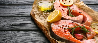 Koyu ahşap zemin üzerinde çiğ somon bifteği, limon, yağ ve baharatlar.