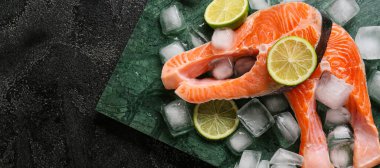 Koyu arkaplanda çiğ somon bifteği, limon ve buz küpleri ve metin için yer var.