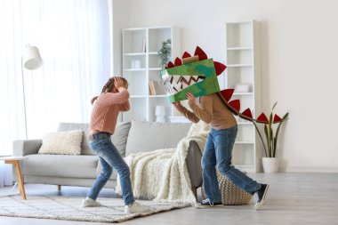 Evde karton dinozor kostümü giymiş korkmuş küçük kız ve kardeşi.