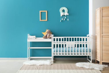 Mavi duvarın yanında oyuncak bebek beşiği ve masa.