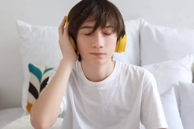 Teenage boy with headphones listening to music in bedroom, closeup