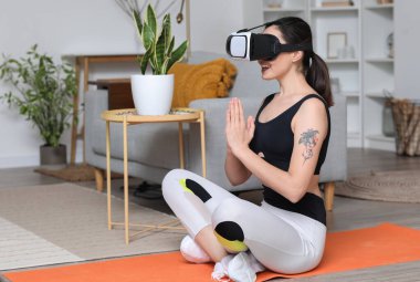 VR gözlüklü genç bir kadın evde meditasyon yapıyor.