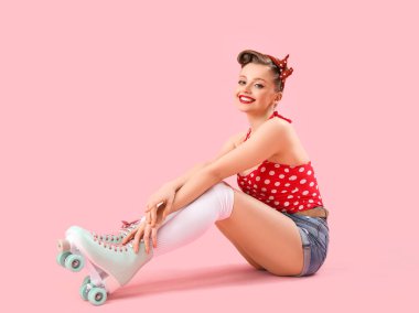Young pin-up woman in roller skates on pink background