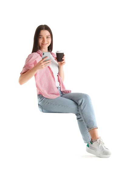 漂亮的年轻女子 拥有现代化的智能手机和咖啡 靠着白色的背景坐在椅子上 — 图库照片