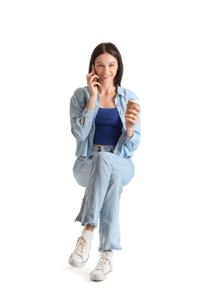 白い背景を背景に椅子に座っている間 スマートフォンで話しているコーヒーを持つかなり若い女性 — ストック写真