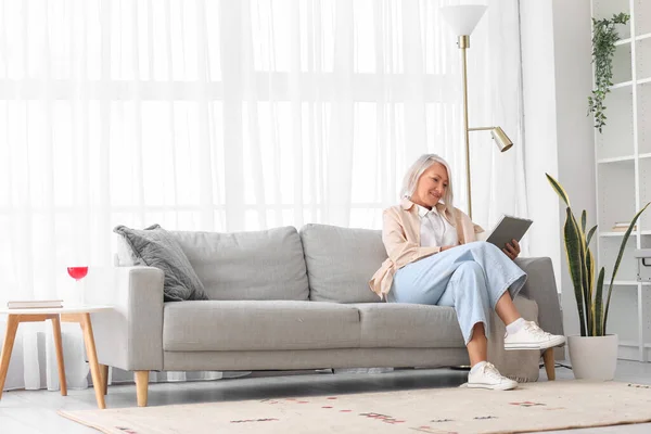 Mature Woman Reading Magazine Grey Sofa Home — Stock Photo, Image