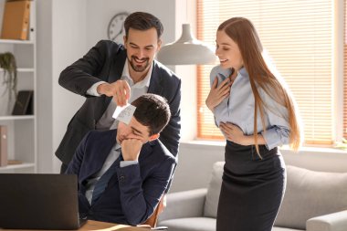 Young man and woman playing a prank on their sleeping colleague in office. April Fools' Day celebration