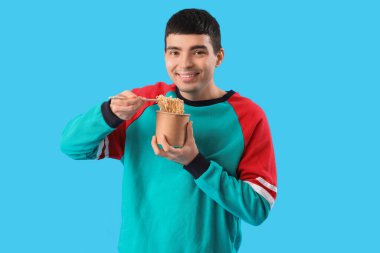 Young man with bowl of Chinese noodles on blue background