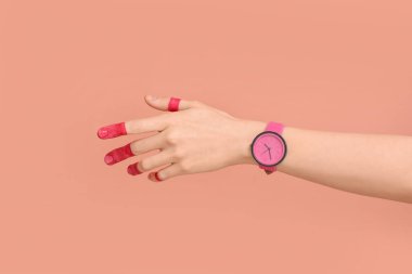 Pembe arka planda boyalı parmakları ve şık kol saati olan bir kadın.