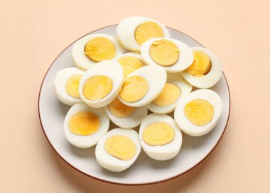 Plate with halves of delicious boiled eggs on beige background