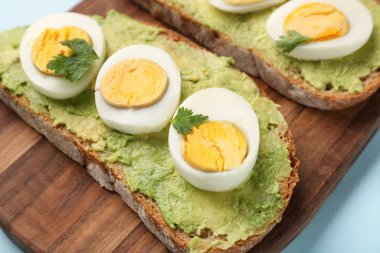 Lezzetli avokado tostları, haşlanmış yumurta, maydanoz ve domatesli mavi arka plan.