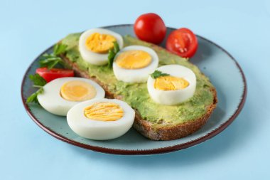 Plate with delicious avocado toast, boiled eggs and tomatoes on blue background