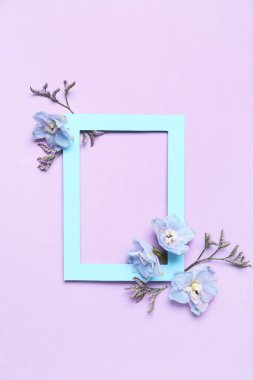 Blank frame and beautiful delphinium flowers on lilac background