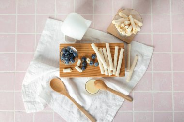 Lezzetli gofret ruloları, yaban mersini ve pembe fayansların üzerine yoğunlaştırılmış süt içeren tahta.