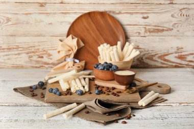 Board with delicious wafer rolls, blueberries and coffee beans on white wooden table