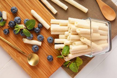 Overturned bowl of delicious wafer rolls and blueberries on white table